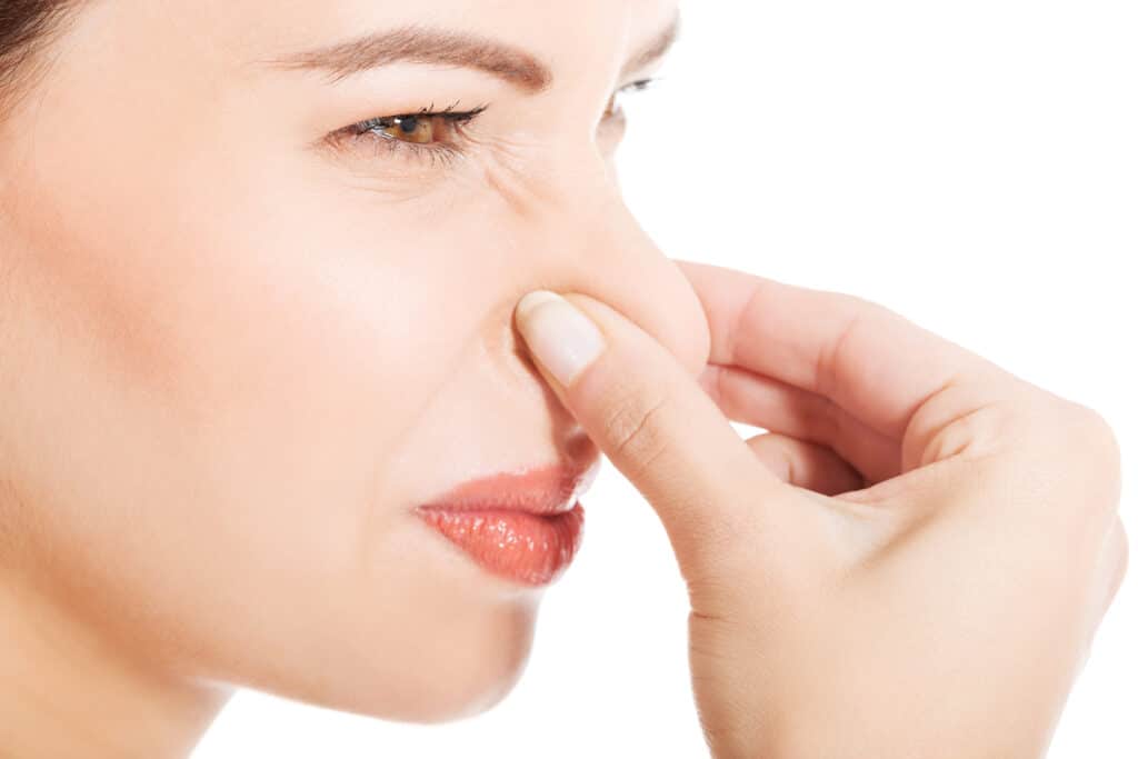 Closeup of a woman plugging her nose with a grimace on her face