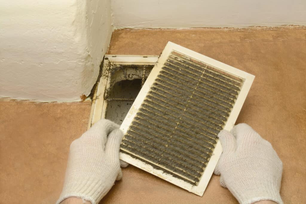 Gloved hands removing a dust-covered vent cover