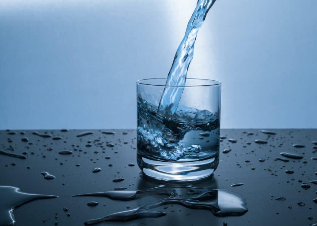 A drinking glass with water being poured into it.