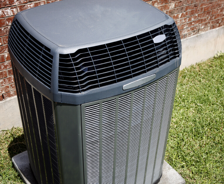 Gray air conditioner on grass next to a brick home.