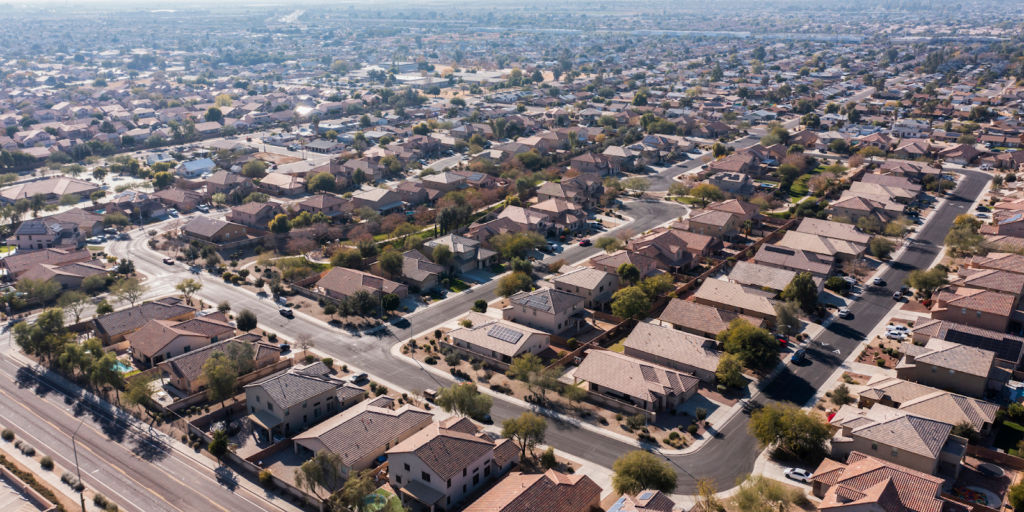 %title% | Penguin Air, Plumbing & Electrical Aerial view of a suburban neighborhood with rows of houses, tree-lined streets, and parked cars, stretching into the distance under a hazy sky.