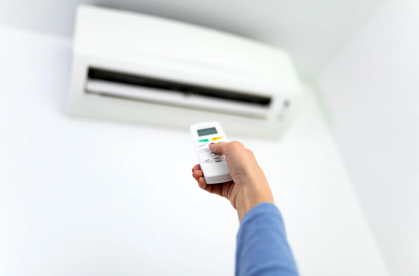 Person holding a remote control aimed at a wall-mounted air conditioner unit.