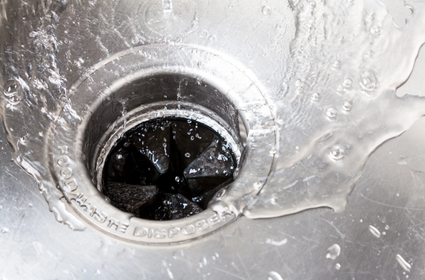 Water flows around the drain of a stainless steel sink with a food waste disposer.