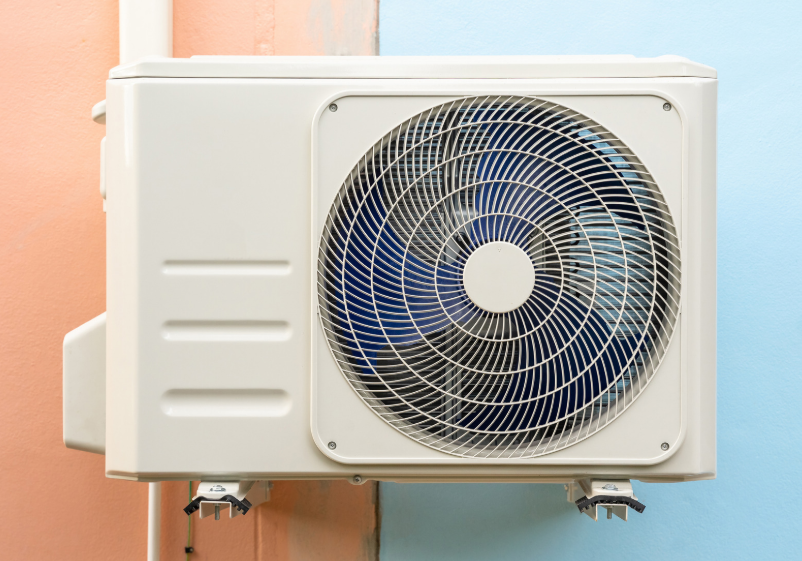 Outdoor air conditioning unit mounted on a wall painted in peach and blue colors.