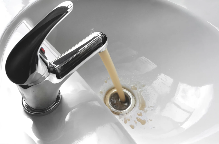 A bathroom sink with brown, murky water flowing from the faucet and draining down.