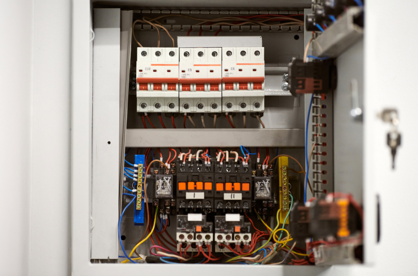 Open electrical control panel showing circuit breakers, switches, relays, and various colored wires connected to terminals and components inside a metal enclosure.