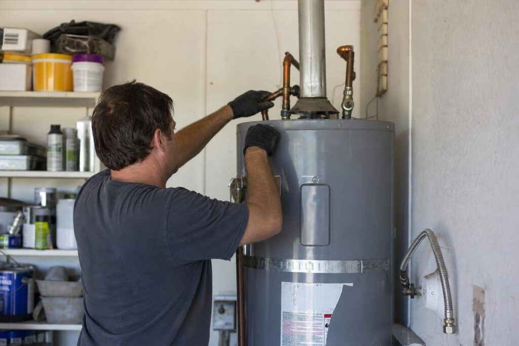 A person wearing gloves repairs or inspects a water heater in a utility room, surrounded by shelves with various containers and tools.